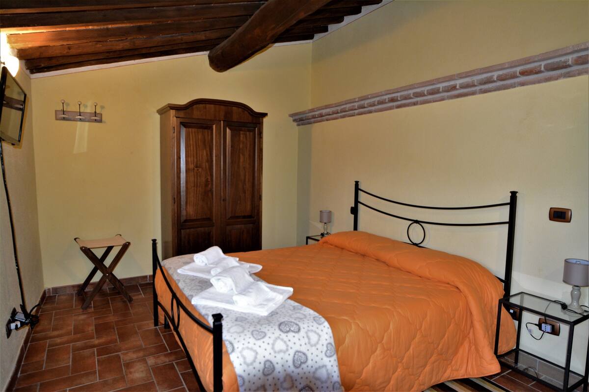 A bedroom with a bed, a wooden wardrobe, a small table with a lamp, and a wall-mounted light fixture.