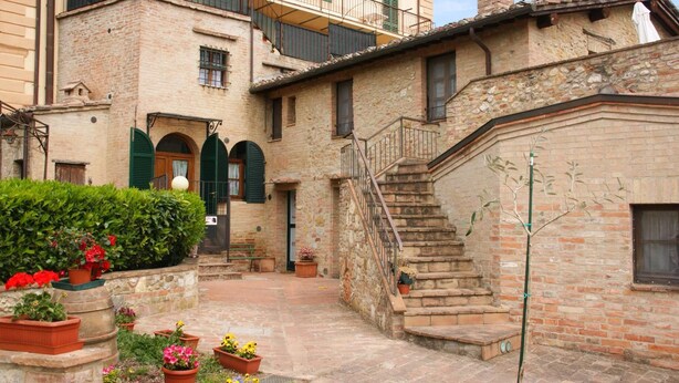 Un bâtiment traditionnel en pierre, doté d’une cour, d’un escalier et de plantes en pot.