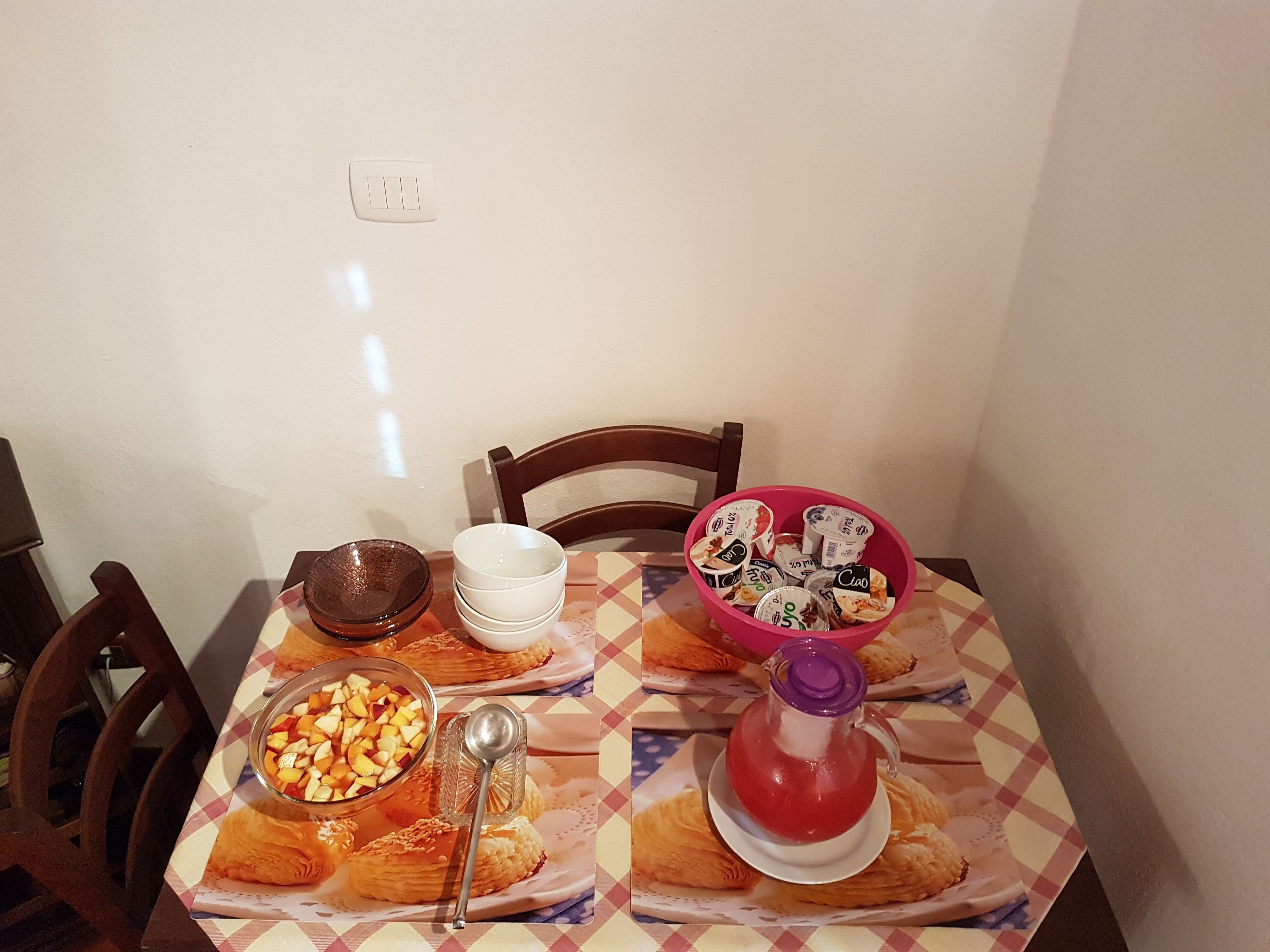 Een eettafel met een geruit tafelkleed, een fruitschaal, een theepot en een bord gebak.