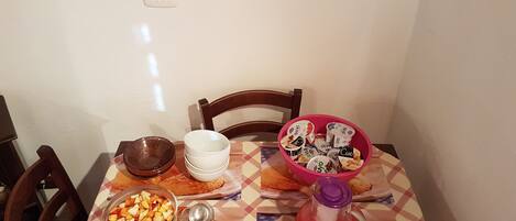 Een eettafel met een geruit tafelkleed, een fruitschaal, een theepot en een bord gebak.
