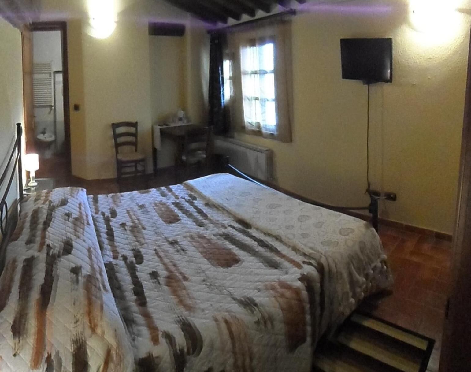 A bedroom with a bed, a desk, a chair, a television, and a window.