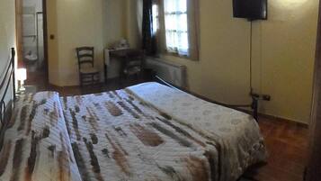 A bedroom with a bed, a desk, a chair, a television, and a window.