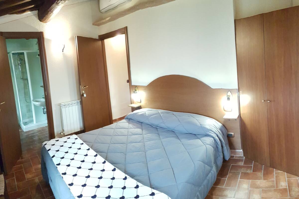 A bedroom with a bed, wooden wardrobe, and a bathroom visible through an open door.