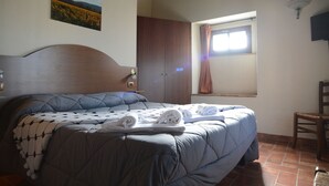 Une chambre avec un grand lit, une tête de lit en bois, un tableau représentant un champ, une fenêtre avec des rideaux et une chaise.