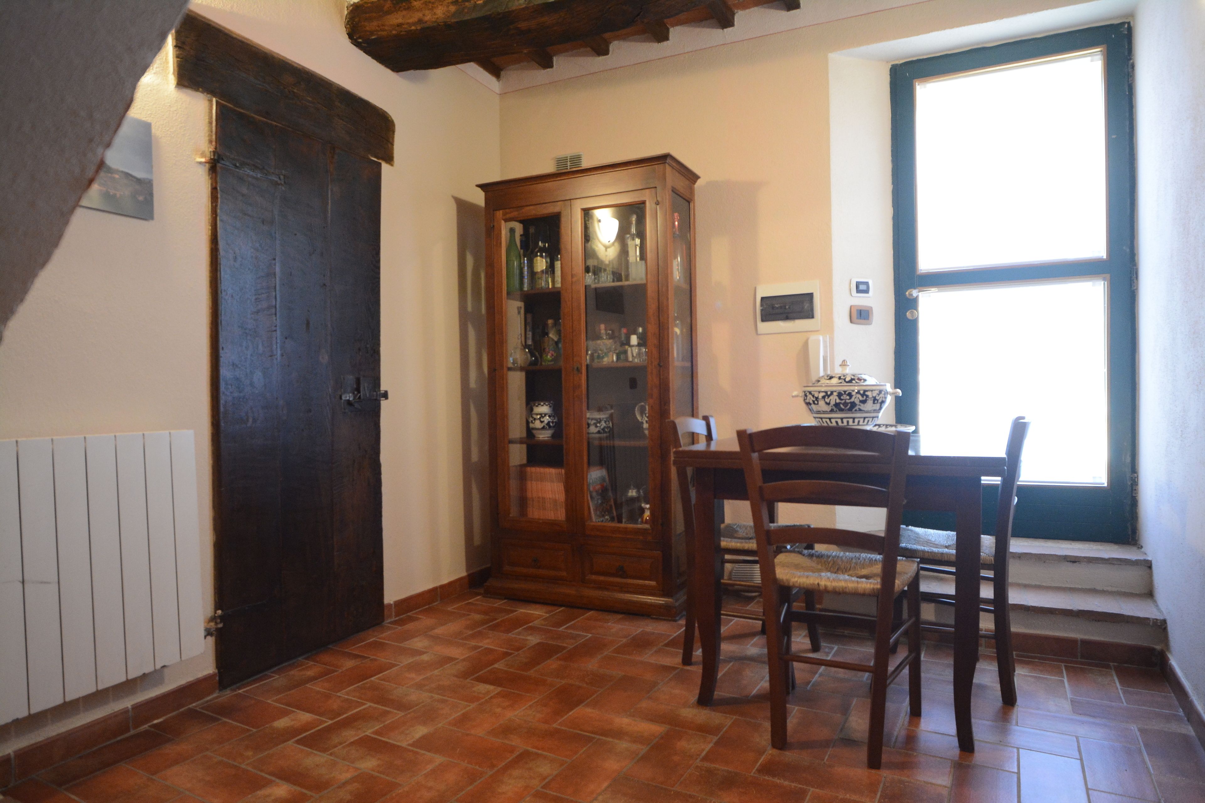 A room with a wooden cabinet, a dining table with chairs, and a window with a view.