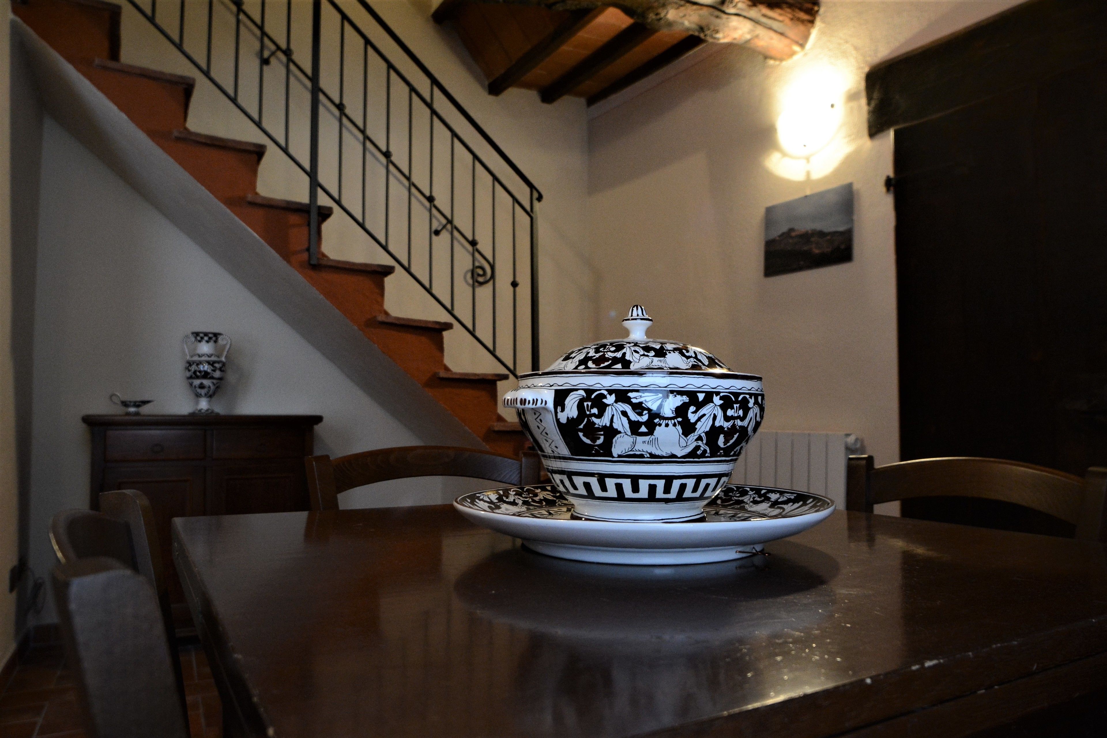 Una mesa de comedor con un cuenco decorativo y un plato, una silla y una escalera al fondo.