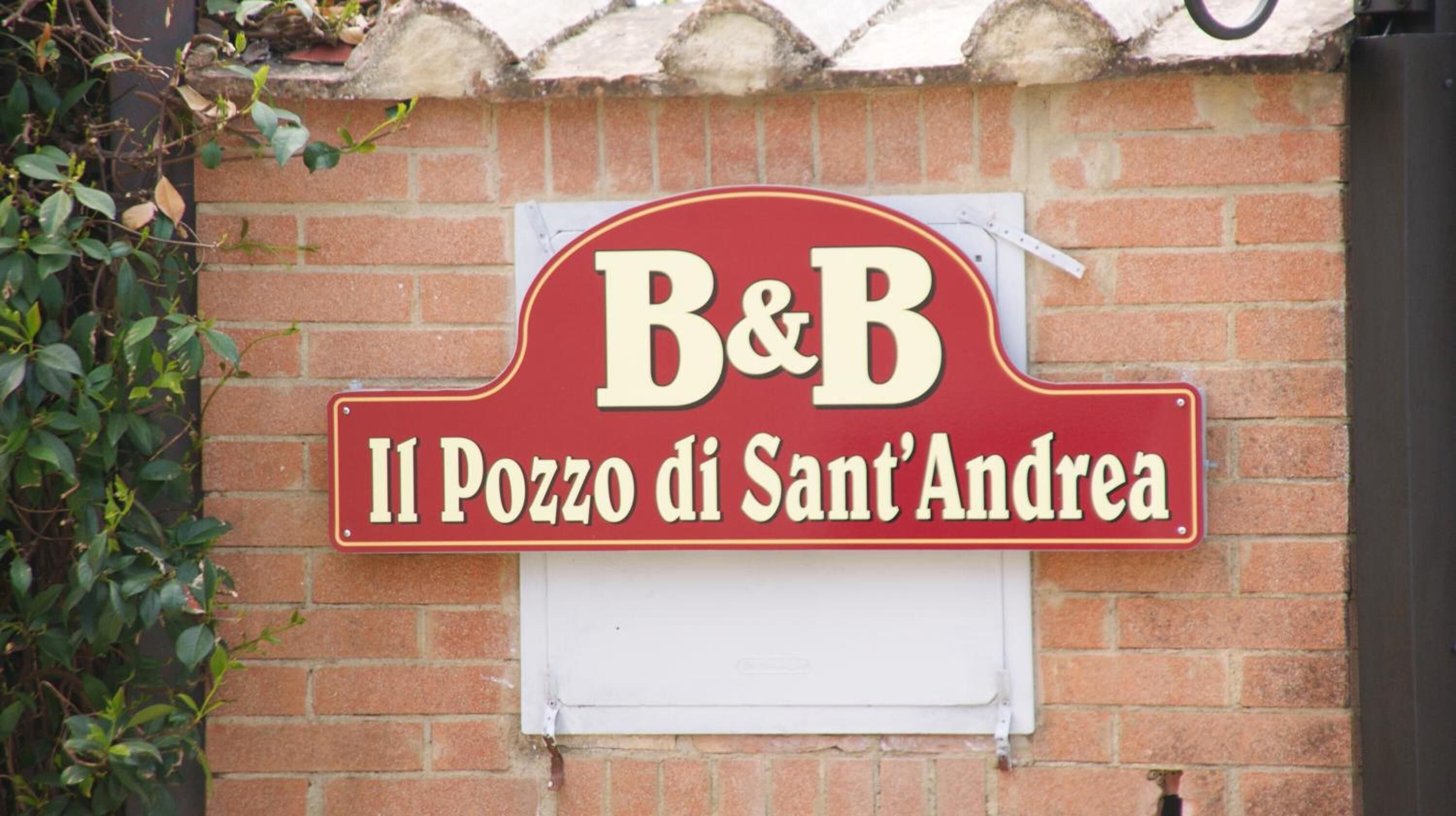 Een rood-wit bord met 'B&B' en 'Il Pozzo di Sant'Andrea' op een bakstenen muur.