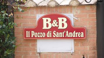 Een rood-wit bord met 'B&B' en 'Il Pozzo di Sant'Andrea' op een bakstenen muur.