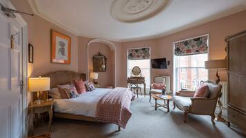 A bedroom with a large bed, two chairs, a desk, and a dresser.