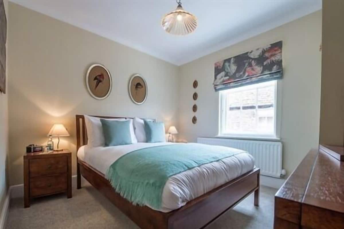 Een slaapkamer met een bed, nachtkastjes, een raam en een plafondlamp.
