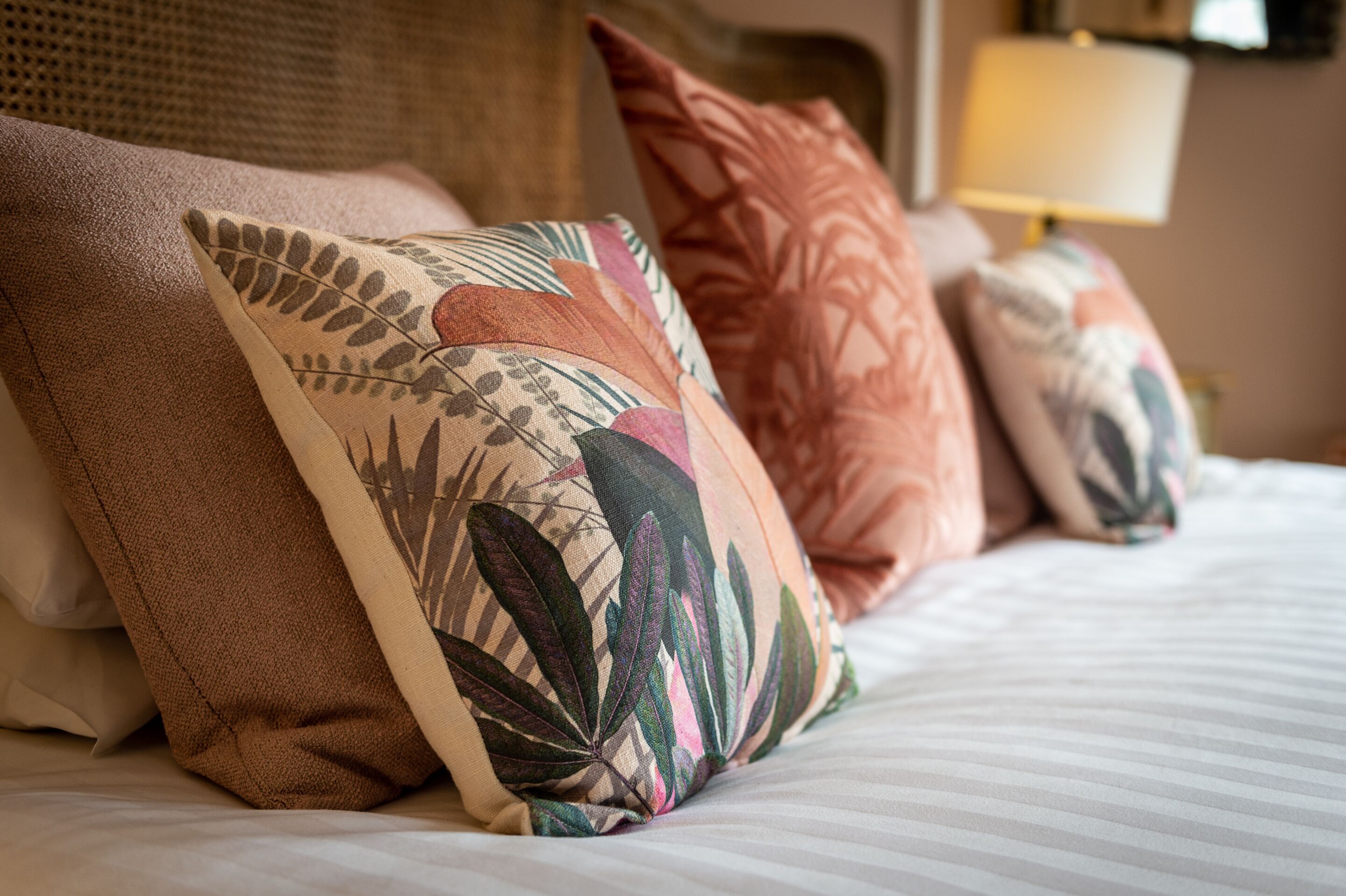 A bed with multiple decorative pillows, a headboard, and a lamp in the background.