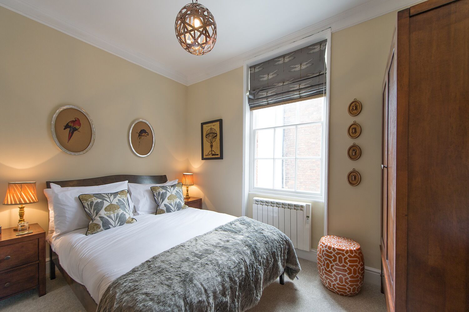 Une chambre à coucher comprenant un lit, des tables de chevet, un radiateur, une fenêtre avec des stores et des éléments de décoration murale.