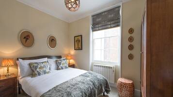 Une chambre à coucher comprenant un lit, des tables de chevet, un radiateur, une fenêtre avec des stores et des éléments de décoration murale.