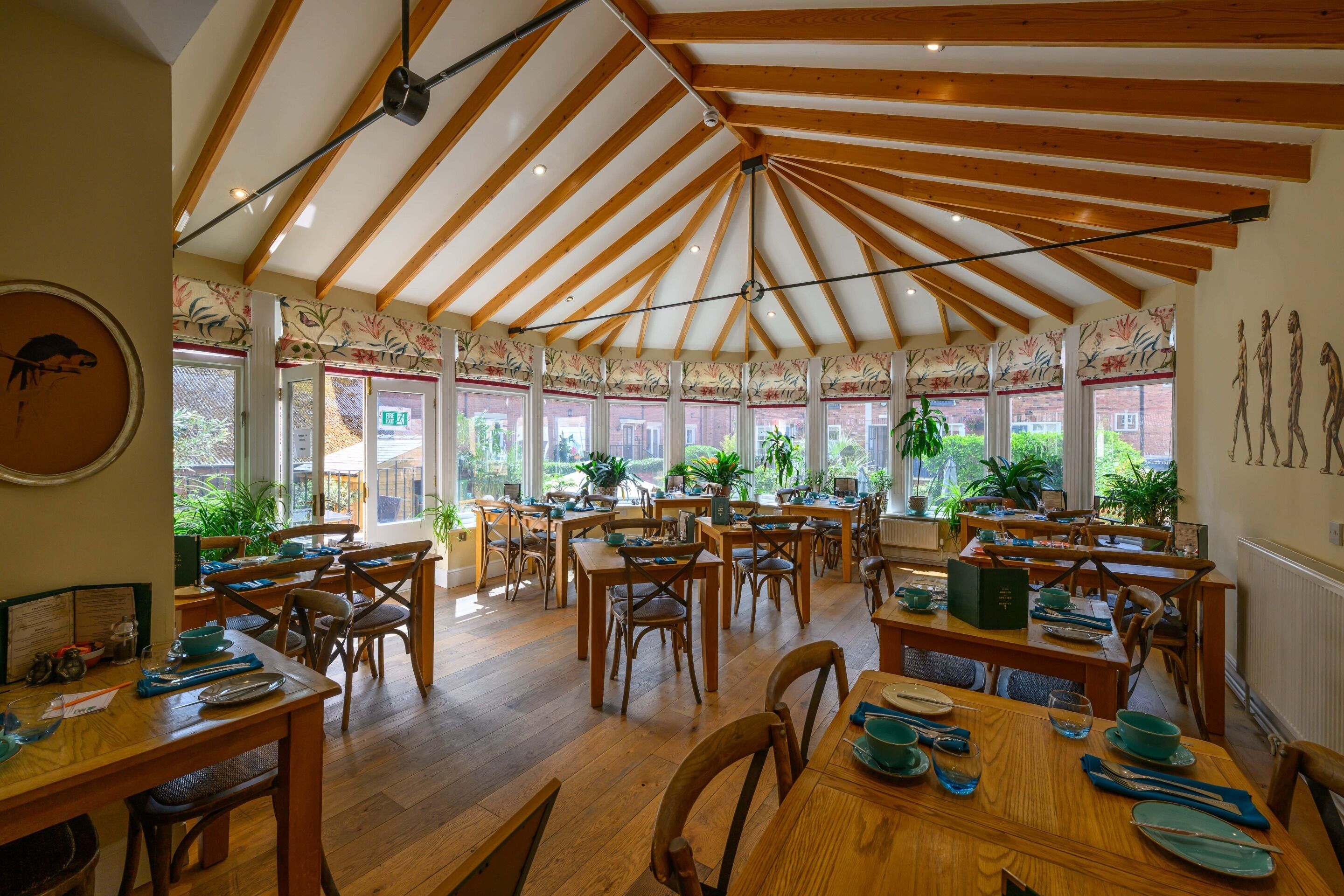 A spacious dining area with wooden tables and chairs, large windows, and a high ceiling with exposed beams.