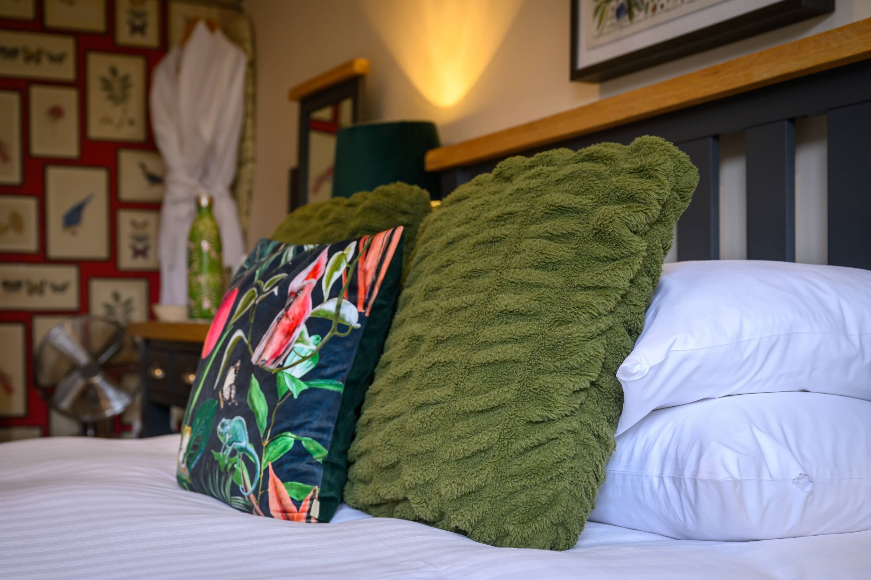 A bed with white pillows and two decorative pillows, one with a floral pattern and the other green.