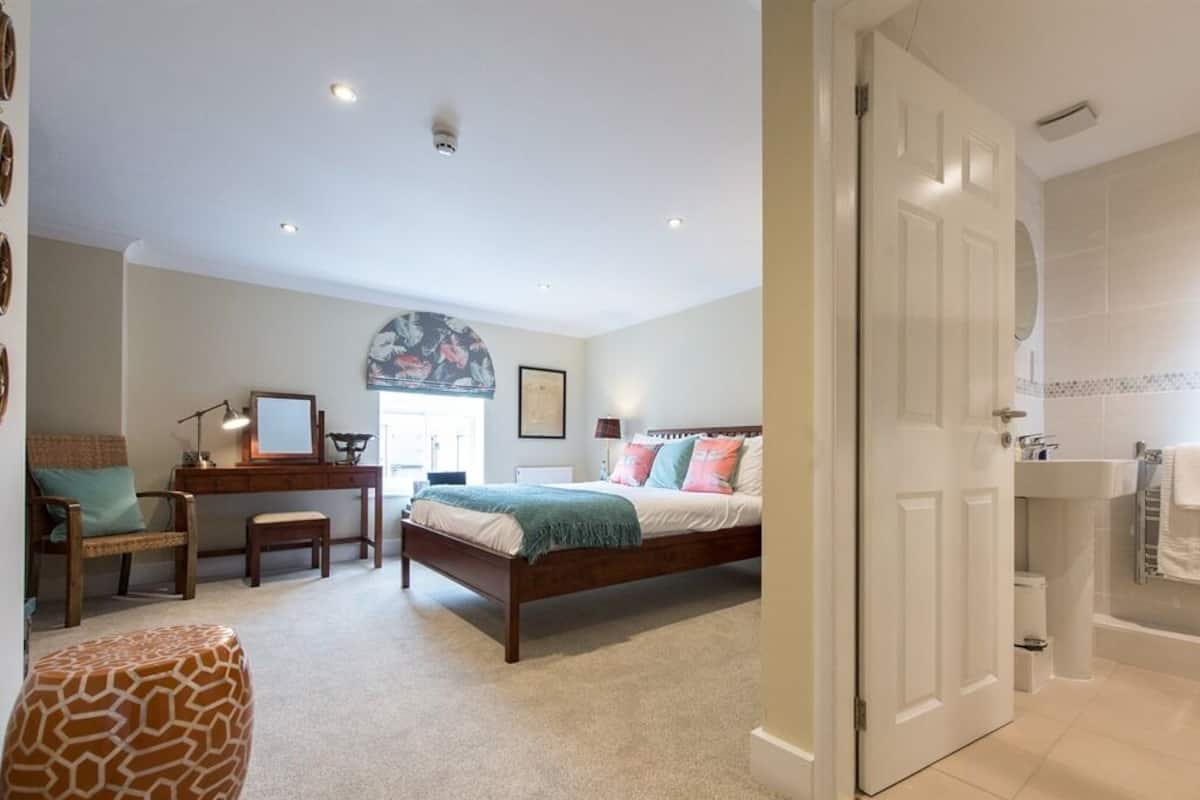 Een slaapkamer met een bed, bureau, stoel en poef.