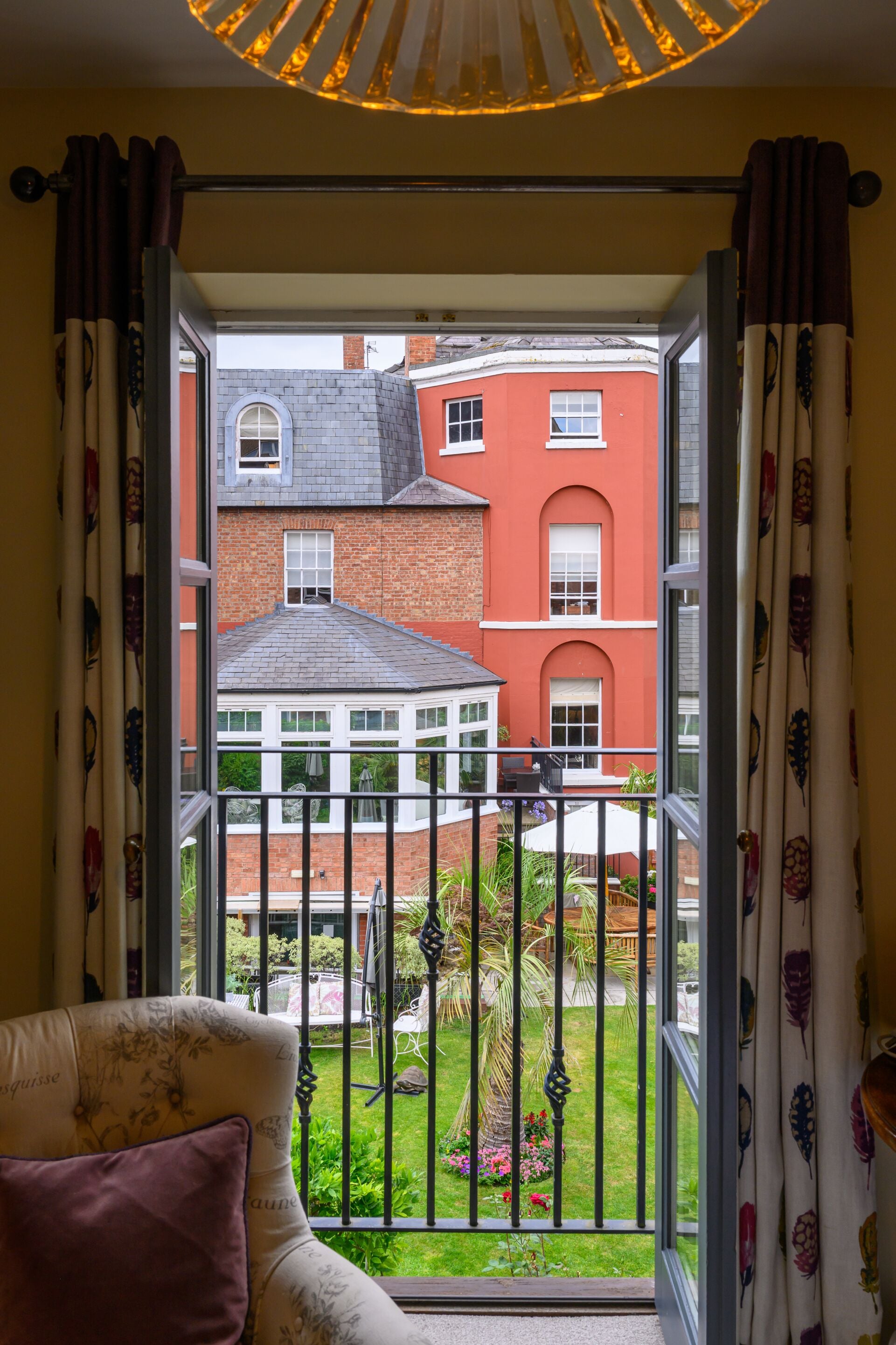 A room with a view of a red brick building through a window with curtains.