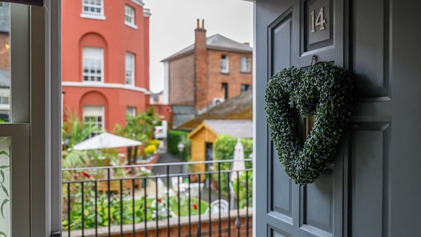 Uitzicht vanaf een balkon met een zwarte deur, een hartvormige krans en een rood gebouw op de achtergrond.