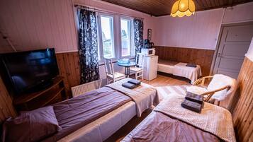 Um quarto acolhedor com duas camas, uma pequena escrivaninha, uma televisão e uma janela com cortinas.