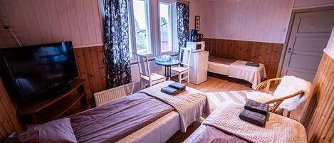 A cozy room with two beds, a small desk, a television, and a window with curtains.