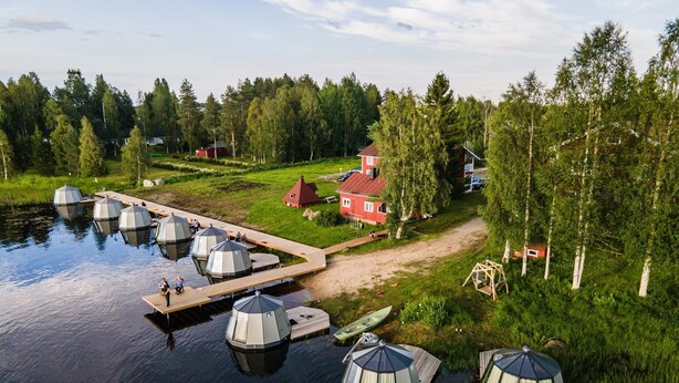 A lakeside property with several dome-shaped structures, a wooden dock, and a red house. - Arctic Guesthouse & Igloos (Ranua)