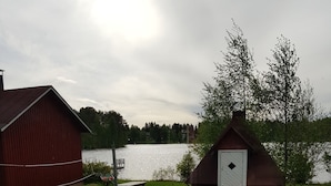 A grassy area with a small wooden structure near a body of water, a red barn, and a picnic table. - Arctic Guesthouse & Igloos (Ranua)