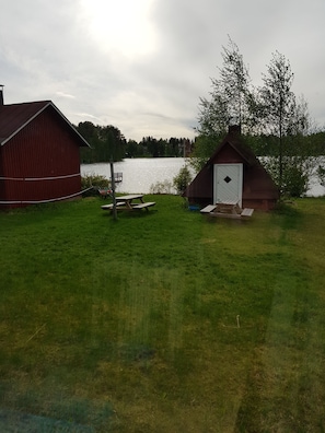 Ruohikkoalue, jonka lähellä on pieni puinen rakennelma, vesistö, punainen lato ja piknikpöytä.
