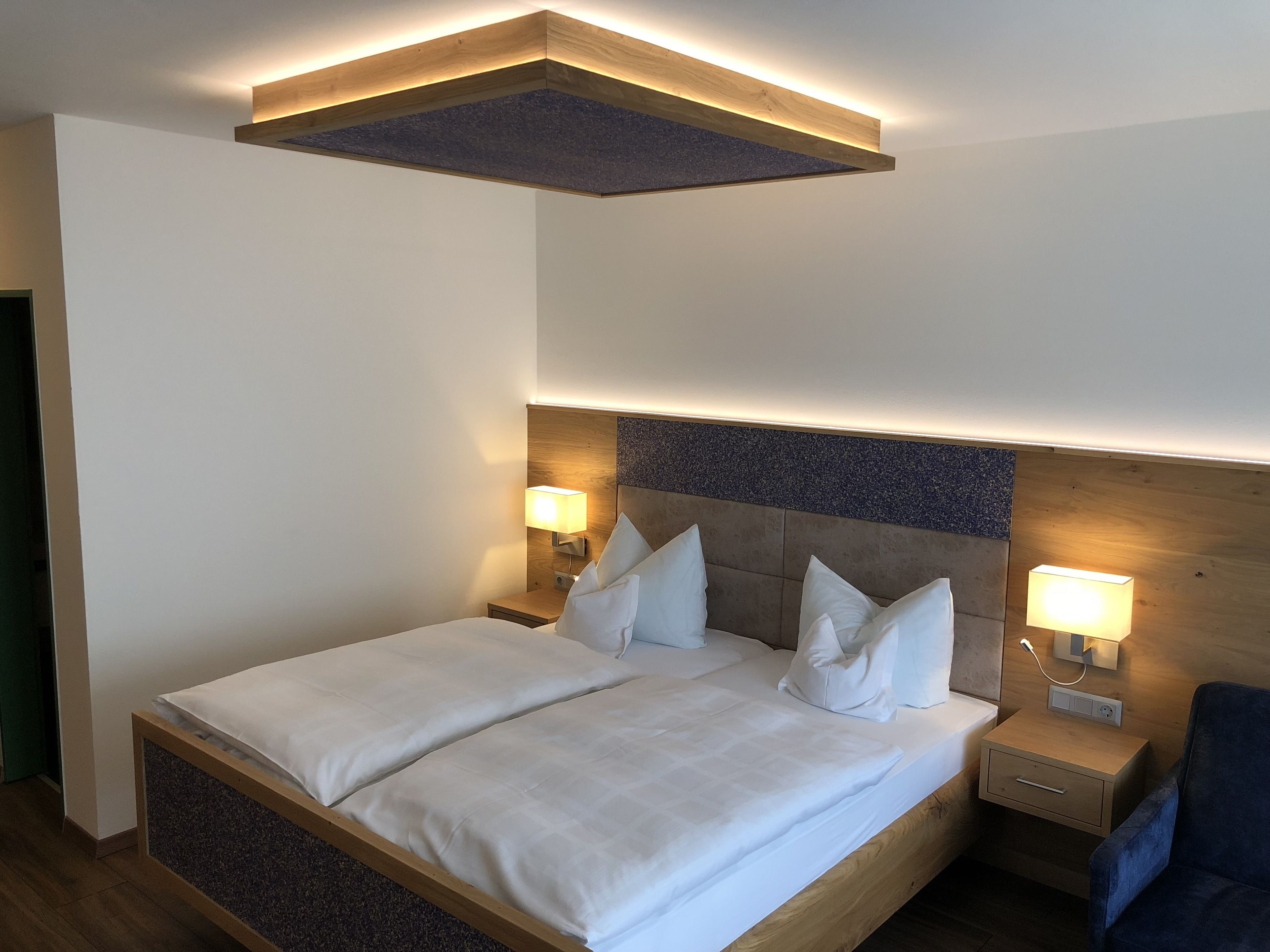 A modern hotel room with a large bed, two bedside tables with lamps, and a wooden headboard.