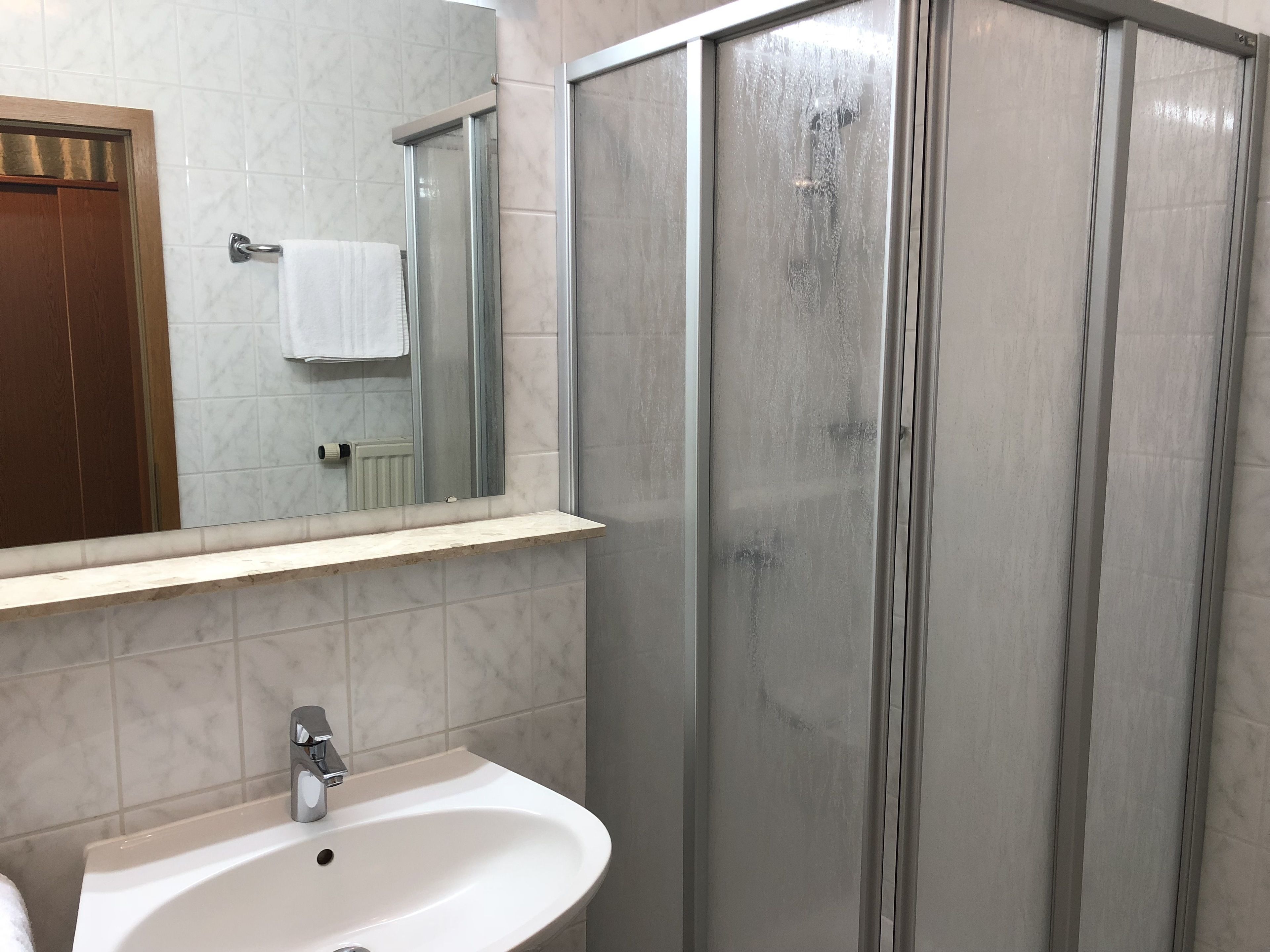 A bathroom with a sink, mirror, and shower enclosure.