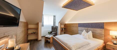 A modern hotel room with a large bed, a desk with a flat-screen TV, a chair, and a small table with a candle.