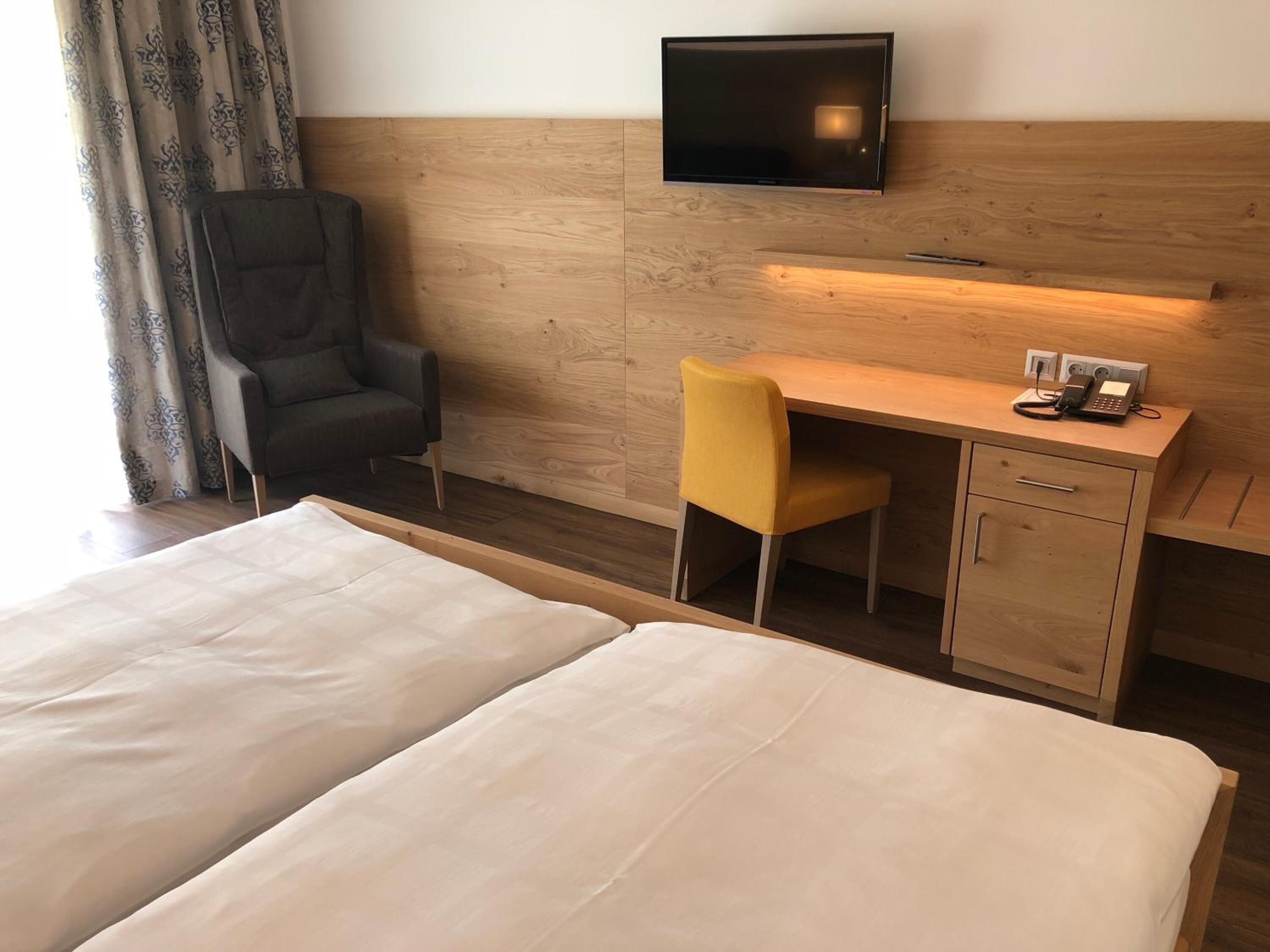 A hotel room with two beds, a desk with a chair, a TV mounted on the wall, and a telephone on the desk.