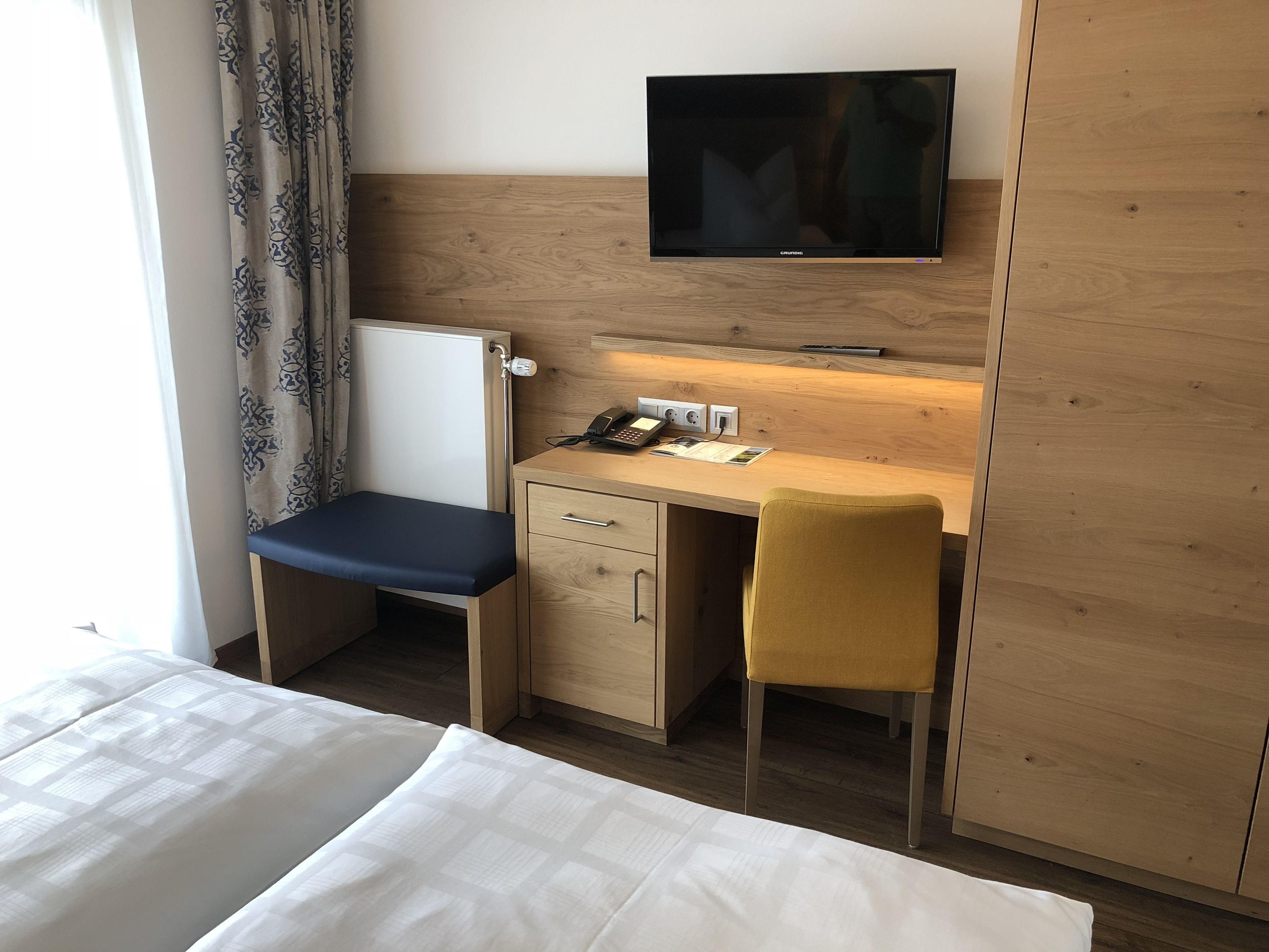 Een hotelkamer met een bed, een bureau met stoel, een televisie en een nachtkastje.