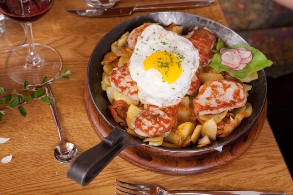 A skillet meal with eggs, sausages, and potatoes on a wooden table.