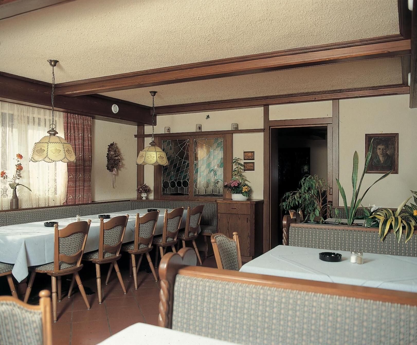 Un comedor con sillas y mesas de madera, una araña y vistas al exterior.