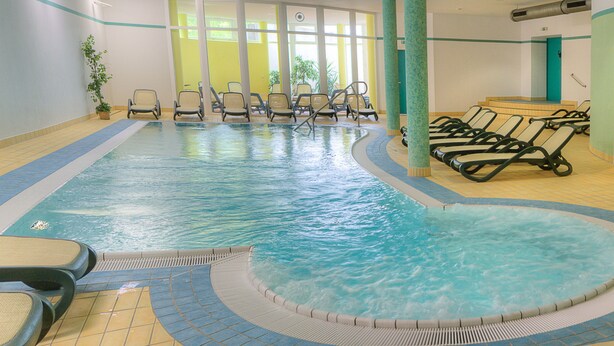 Una piscina interior con varias sillas reclinables y suelo de baldosas.