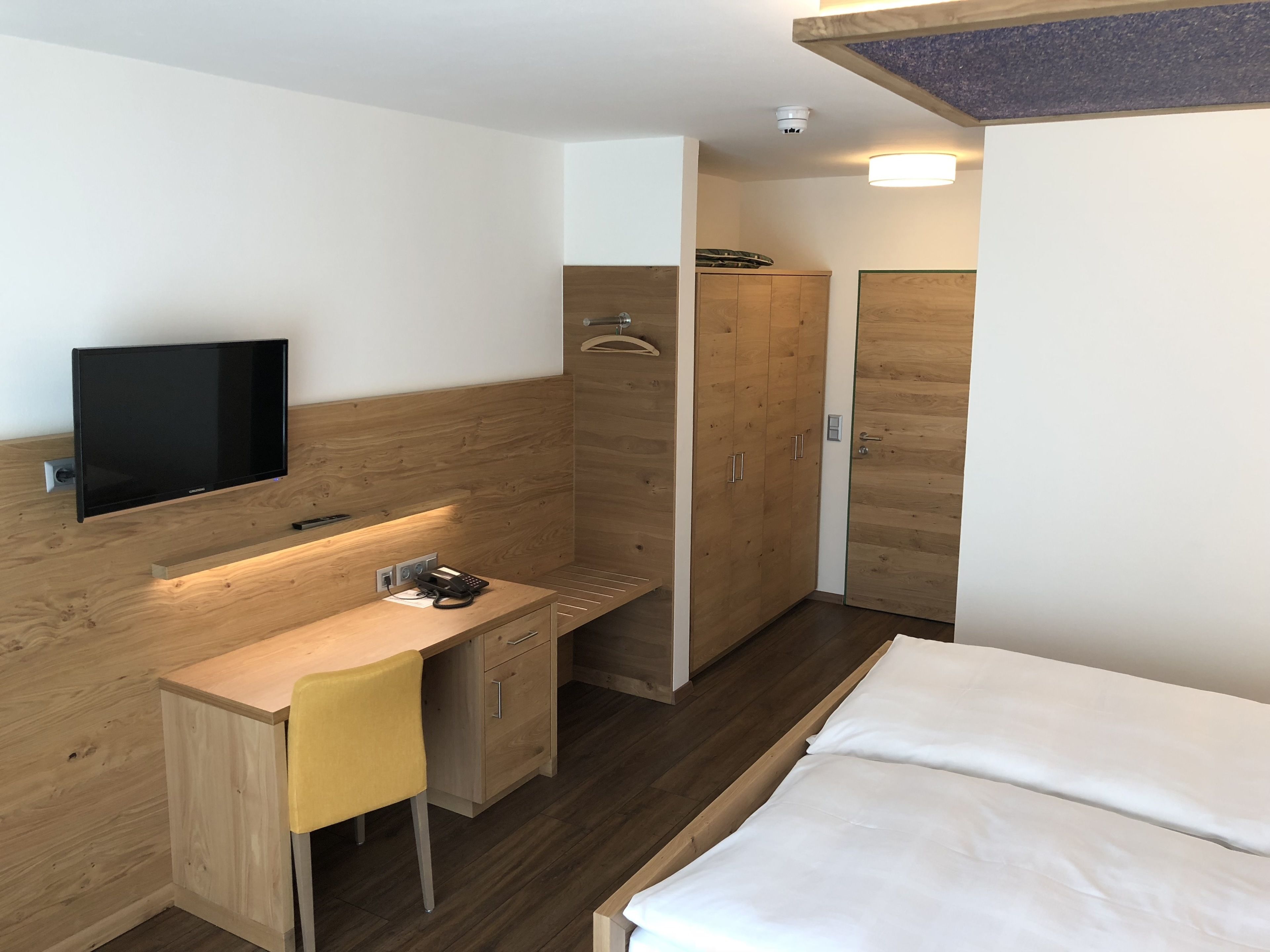 Une chambre d’hôtel moderne équipée d’un bureau en bois, d’un téléviseur à écran plat, d’un lit et d’une armoire.