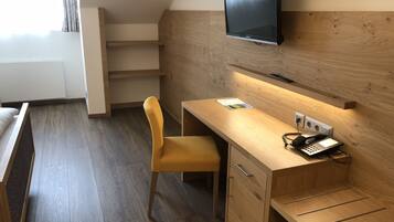 Una habitación de hotel moderna con un escritorio de madera, una silla, un televisor de pantalla plana montado en la pared y un teléfono.
