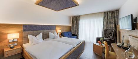 A hotel room with a large bed, a desk, a chair, a TV, and a window with curtains.