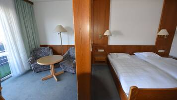 A hotel room with a bed, a chair, a small table, and two wall-mounted lamps.