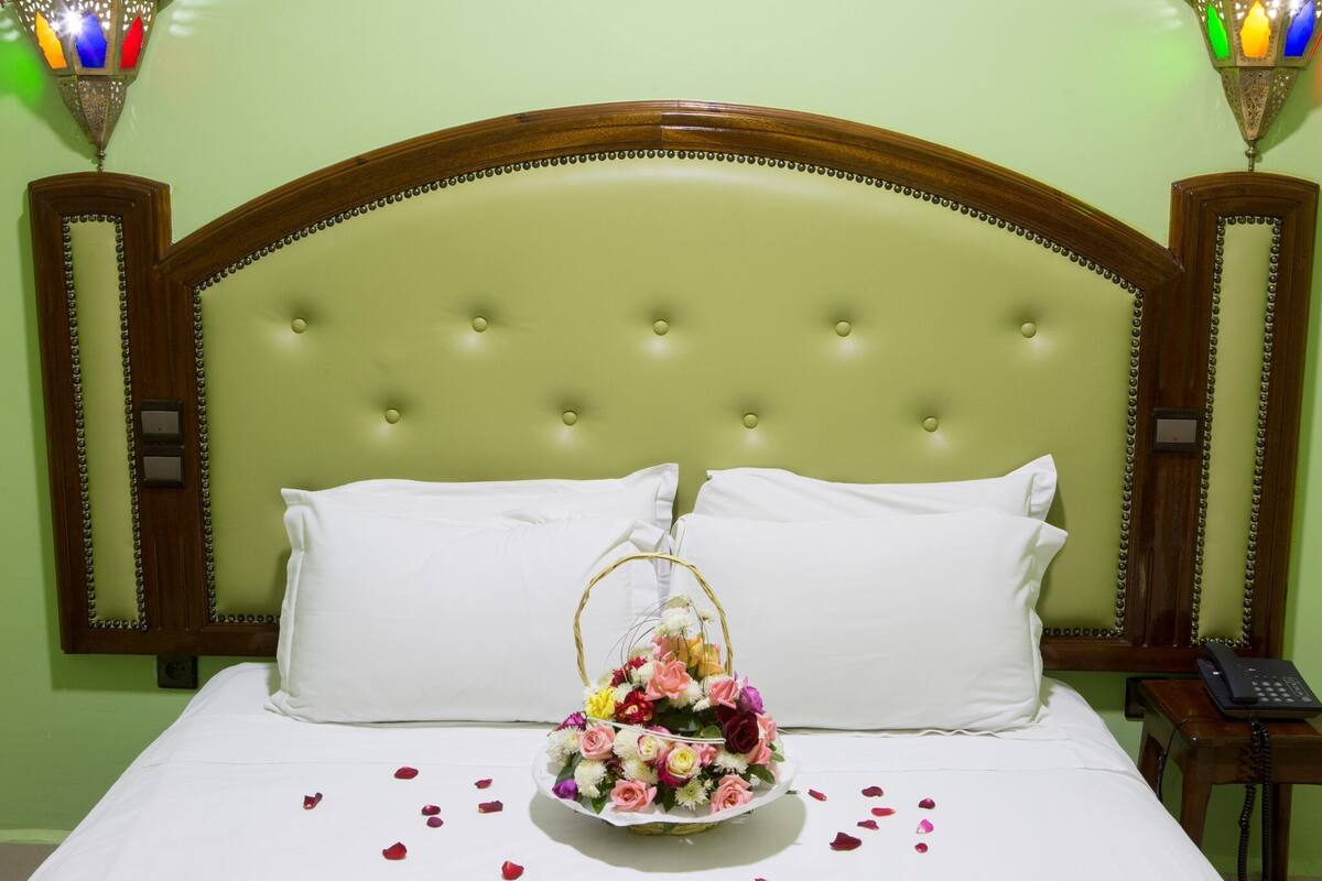 A neatly made bed with white linens, a floral arrangement in a basket, and a bedside telephone.