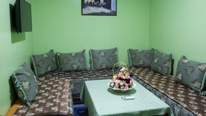 A room with a green wall, a sofa with patterned cushions, a small table with a floral arrangement, and a framed picture above the sofa. - Hôtel Résidence Amalou (Marrakech)