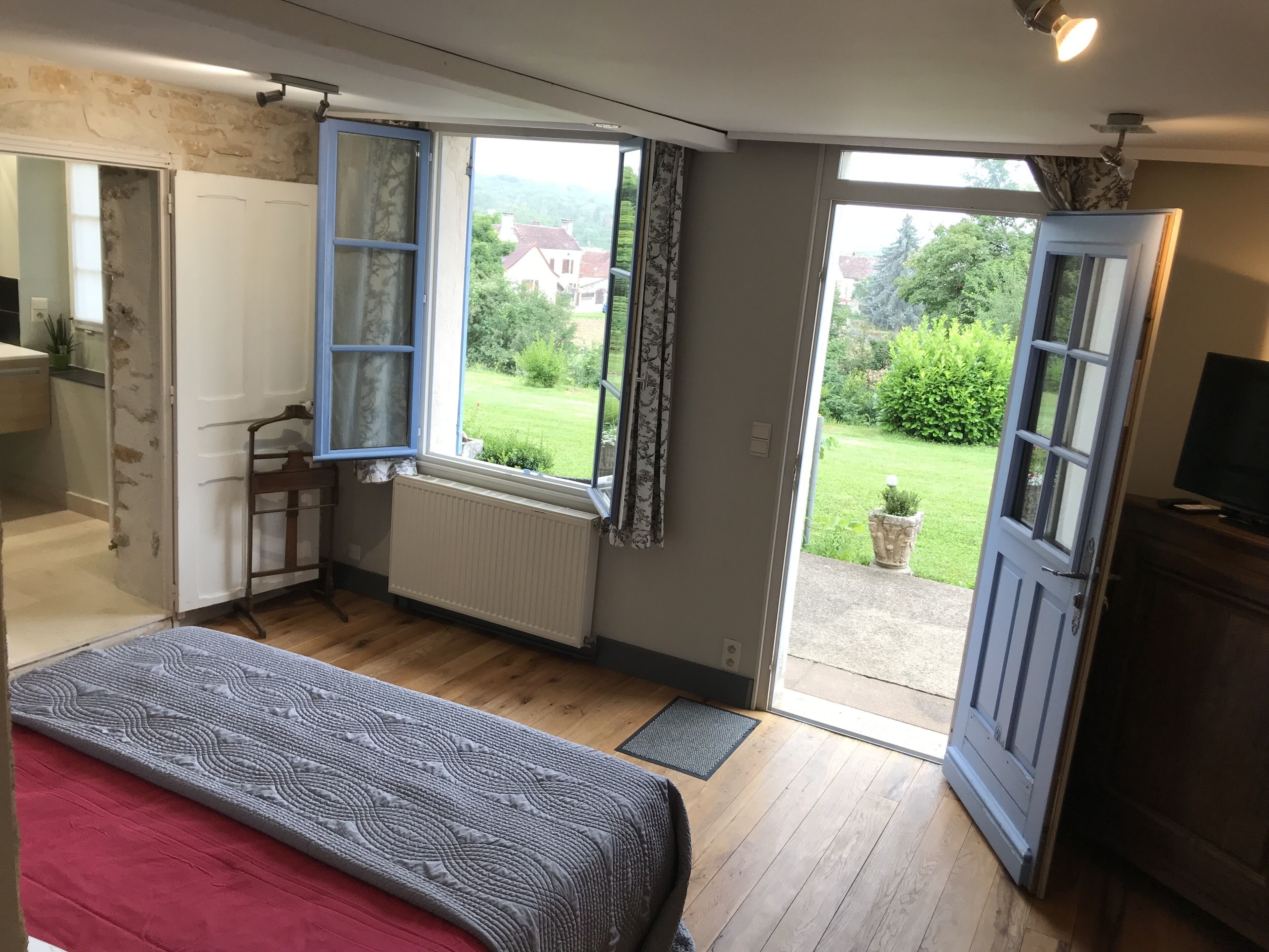 A bedroom with a bed, a window, and a view of a garden.
