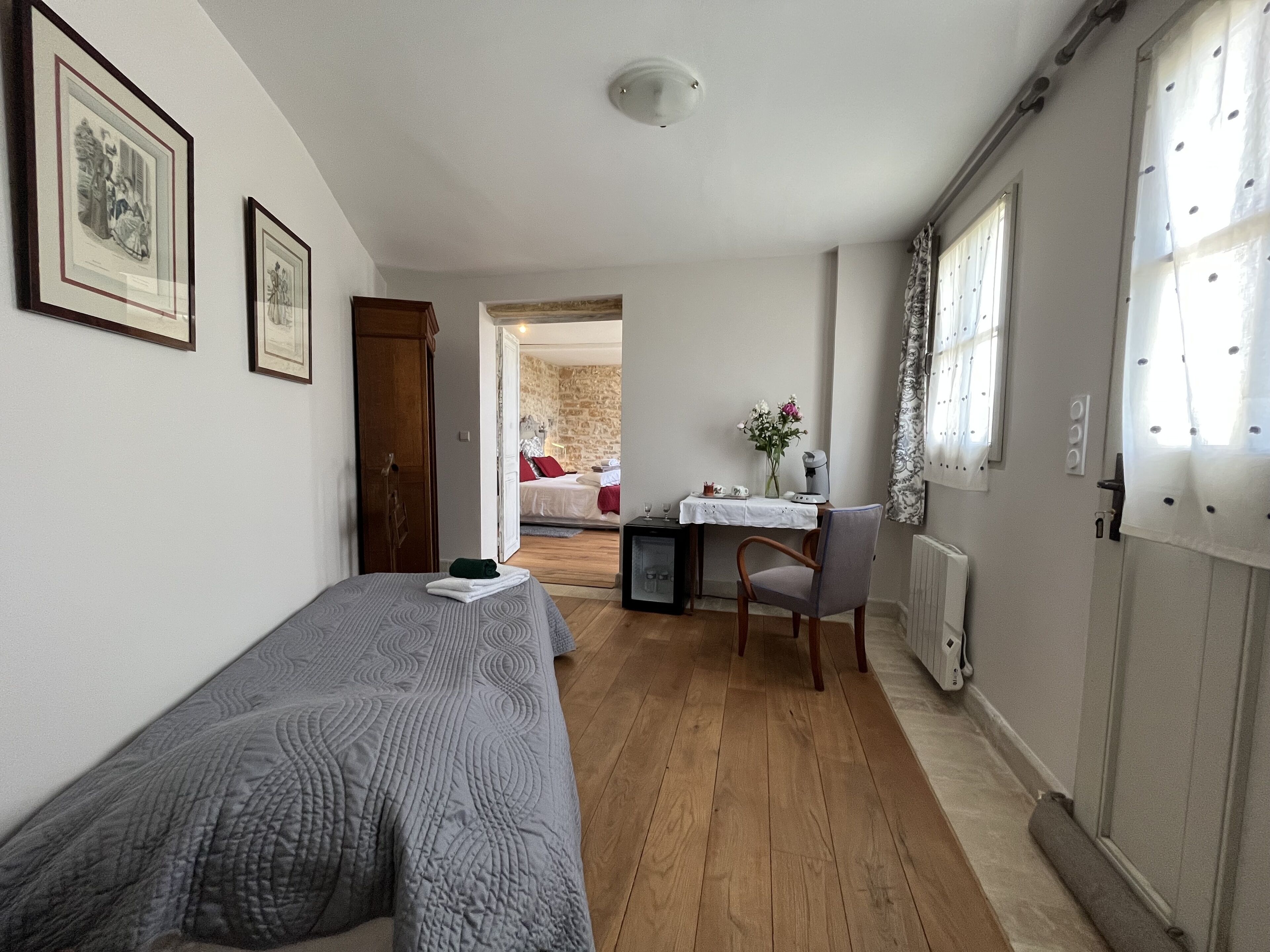 A room with a bed, a desk with a chair, a radiator, and framed pictures on the wall.