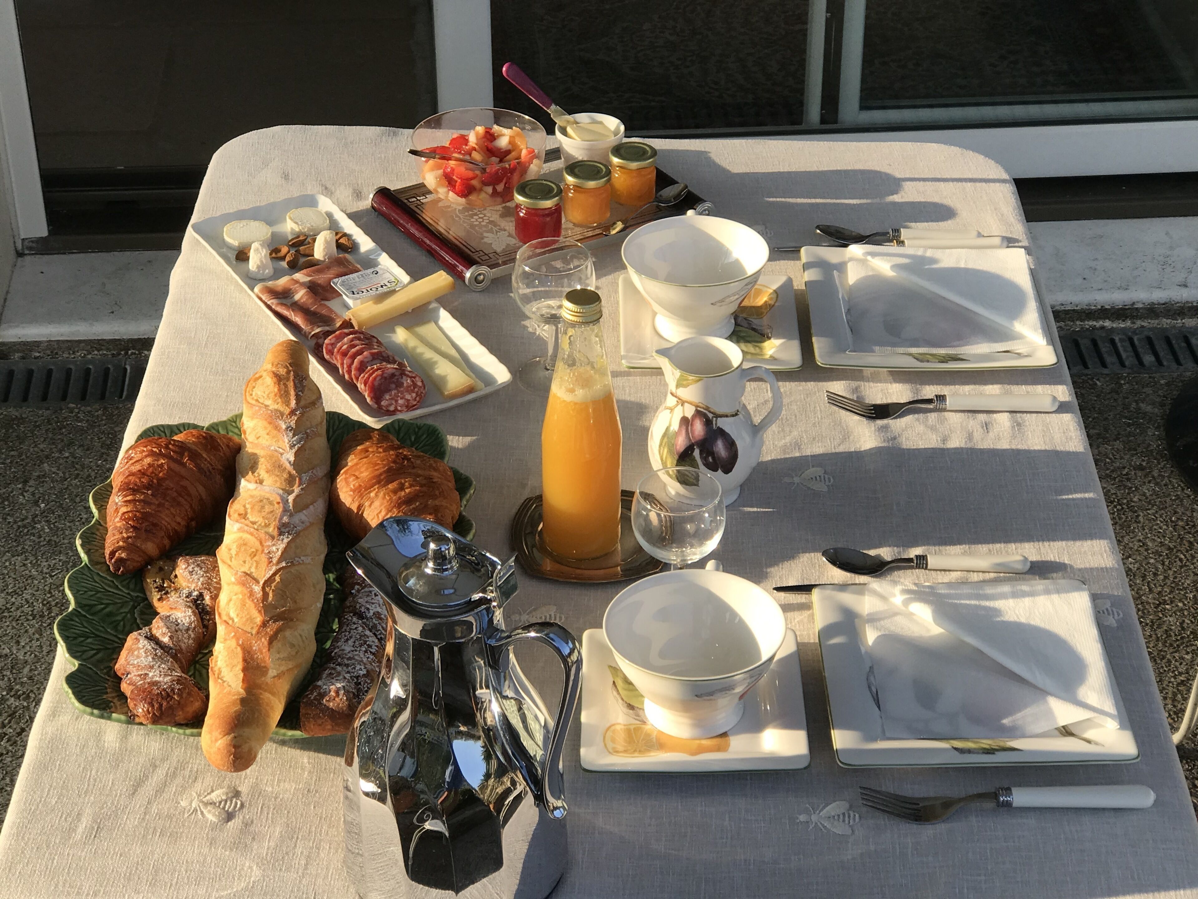 Une table dressée avec une variété de plats, notamment des pâtisseries, du fromage et de la charcuterie, ainsi que des boissons et des couverts.