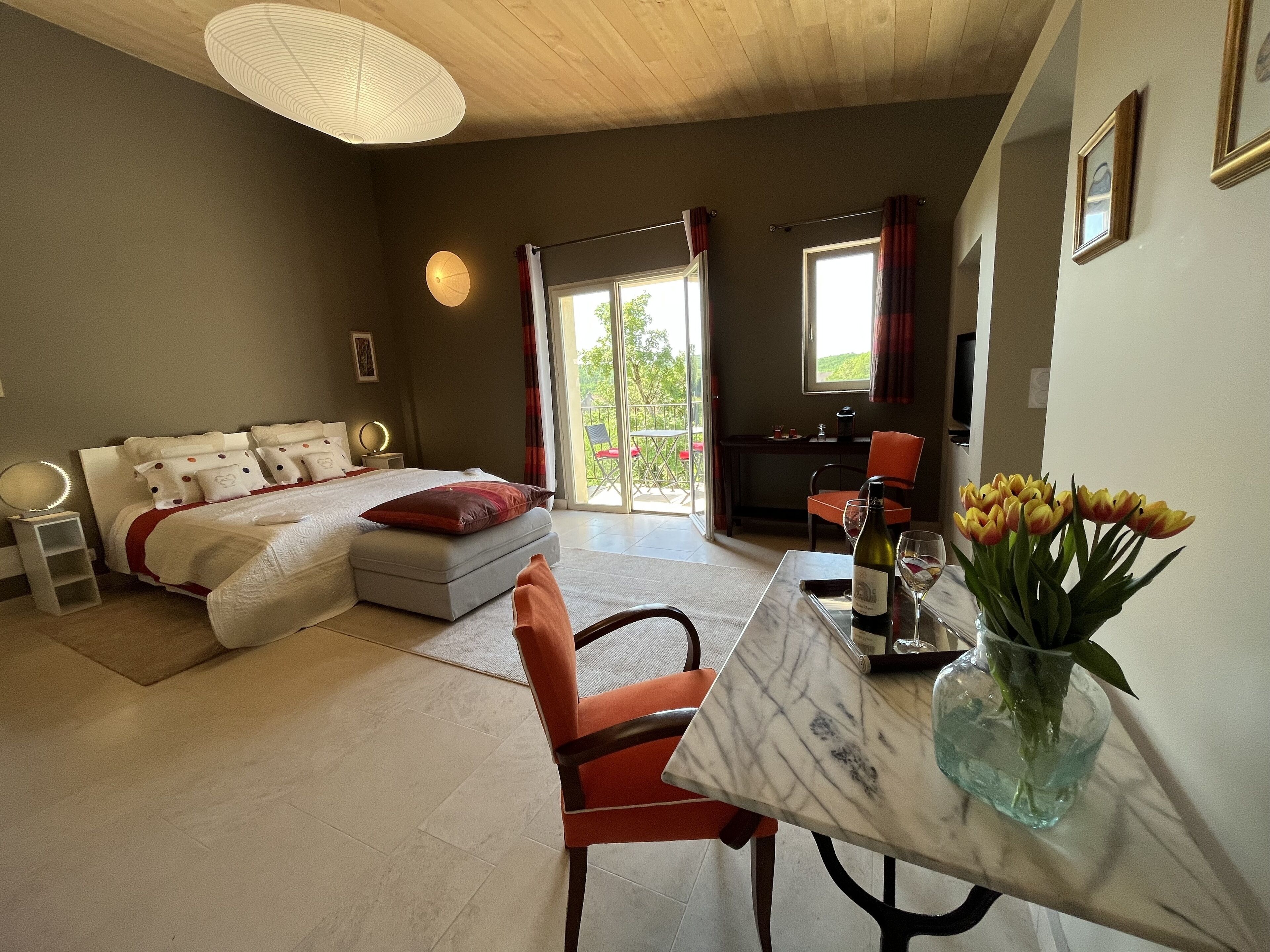 A bedroom with a bed, a table with a vase of flowers, and a view of the outdoors.