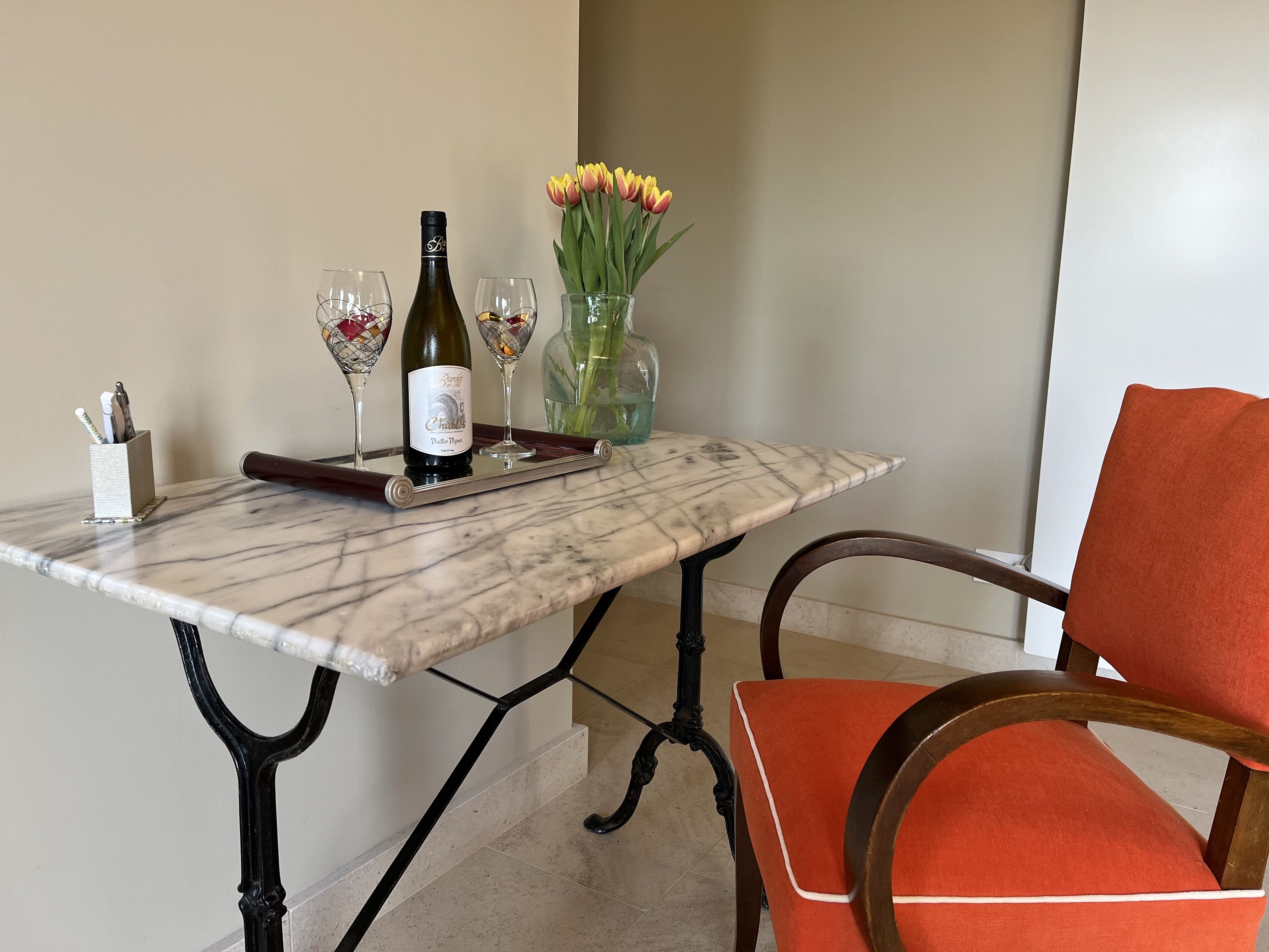 A marble table with a bottle of wine, glasses, and a vase with flowers.
