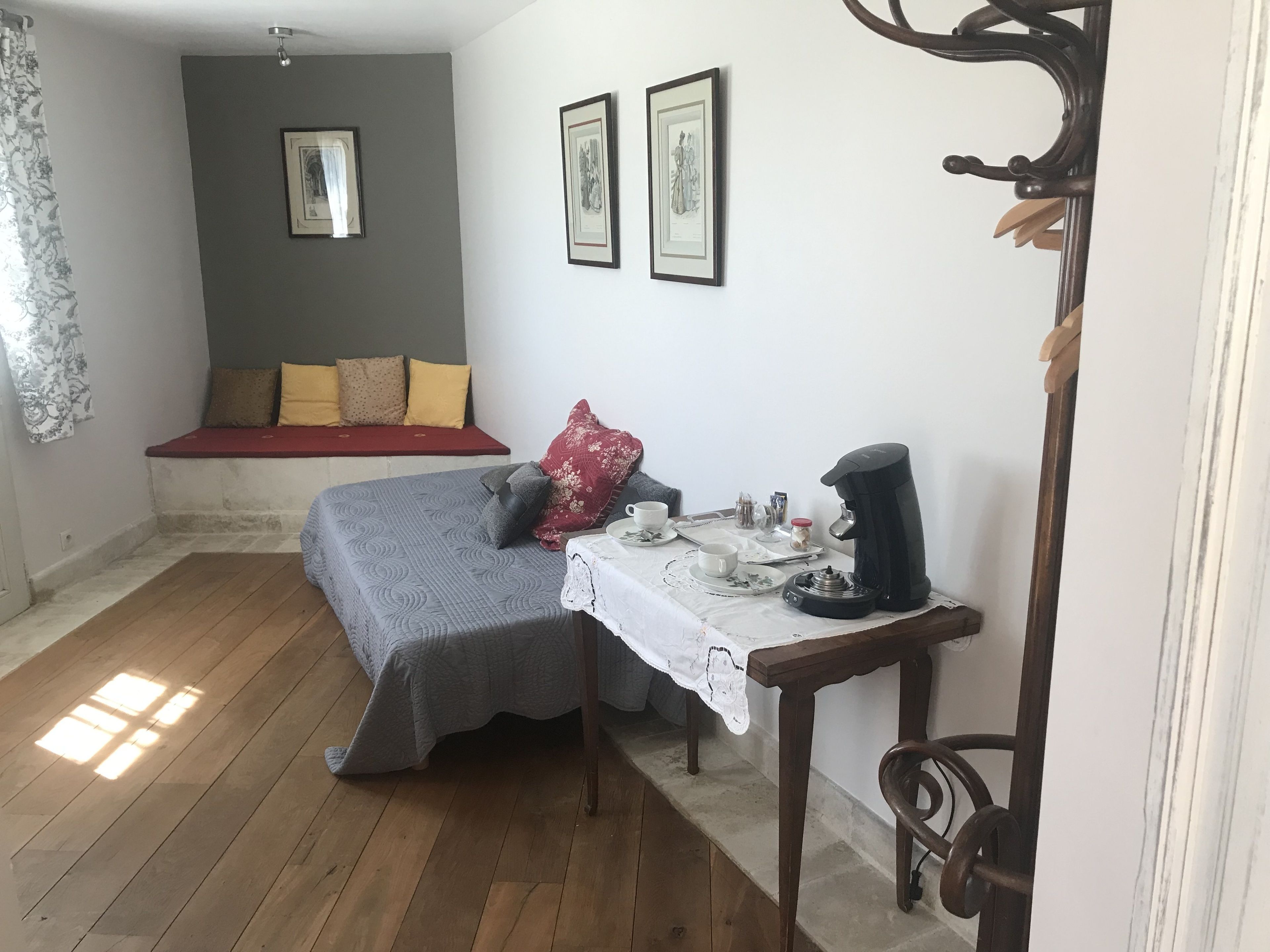 Una habitación pequeña y acogedora con una cama, una mesa con cafetera y dos cuadros en la pared.