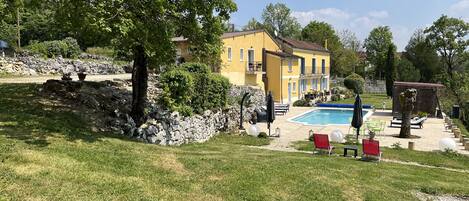 A yellow villa with a swimming pool, stone walls, and outdoor seating.