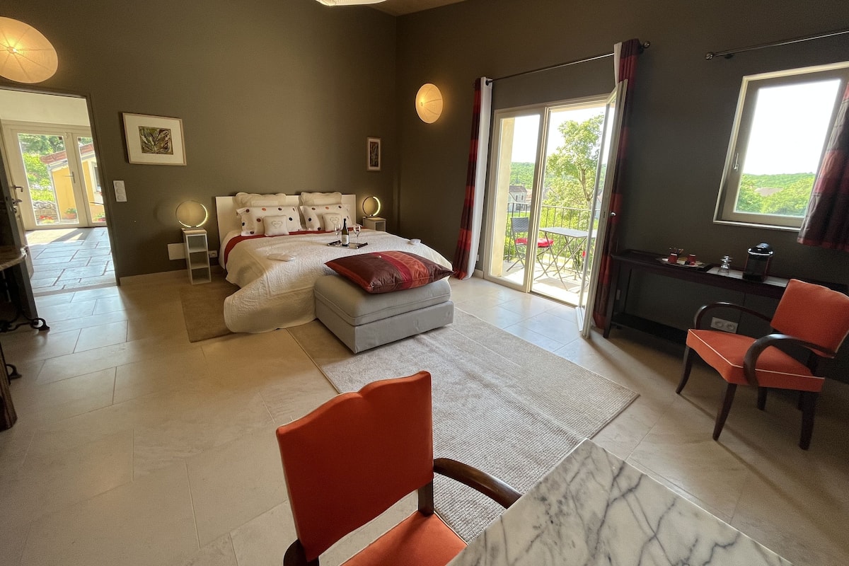 A bedroom with a bed, a desk, a chair, and a large window.
