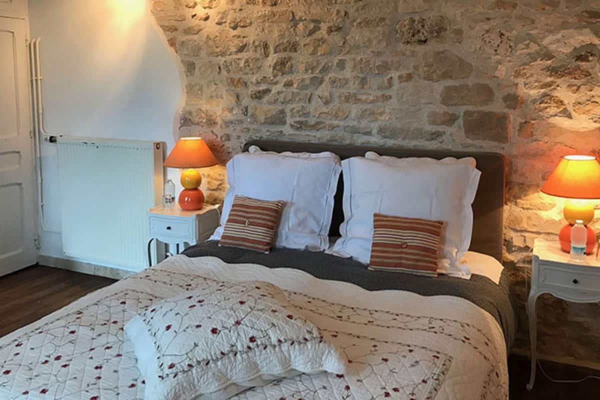 A bedroom with a stone wall, a bed with white bedding, two bedside tables with lamps, and a radiator.